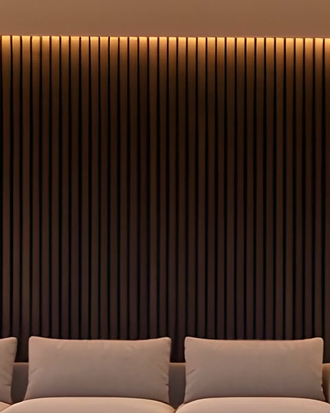 Dark timber slats lit by a warm cove, above the backs of a pale sofa.